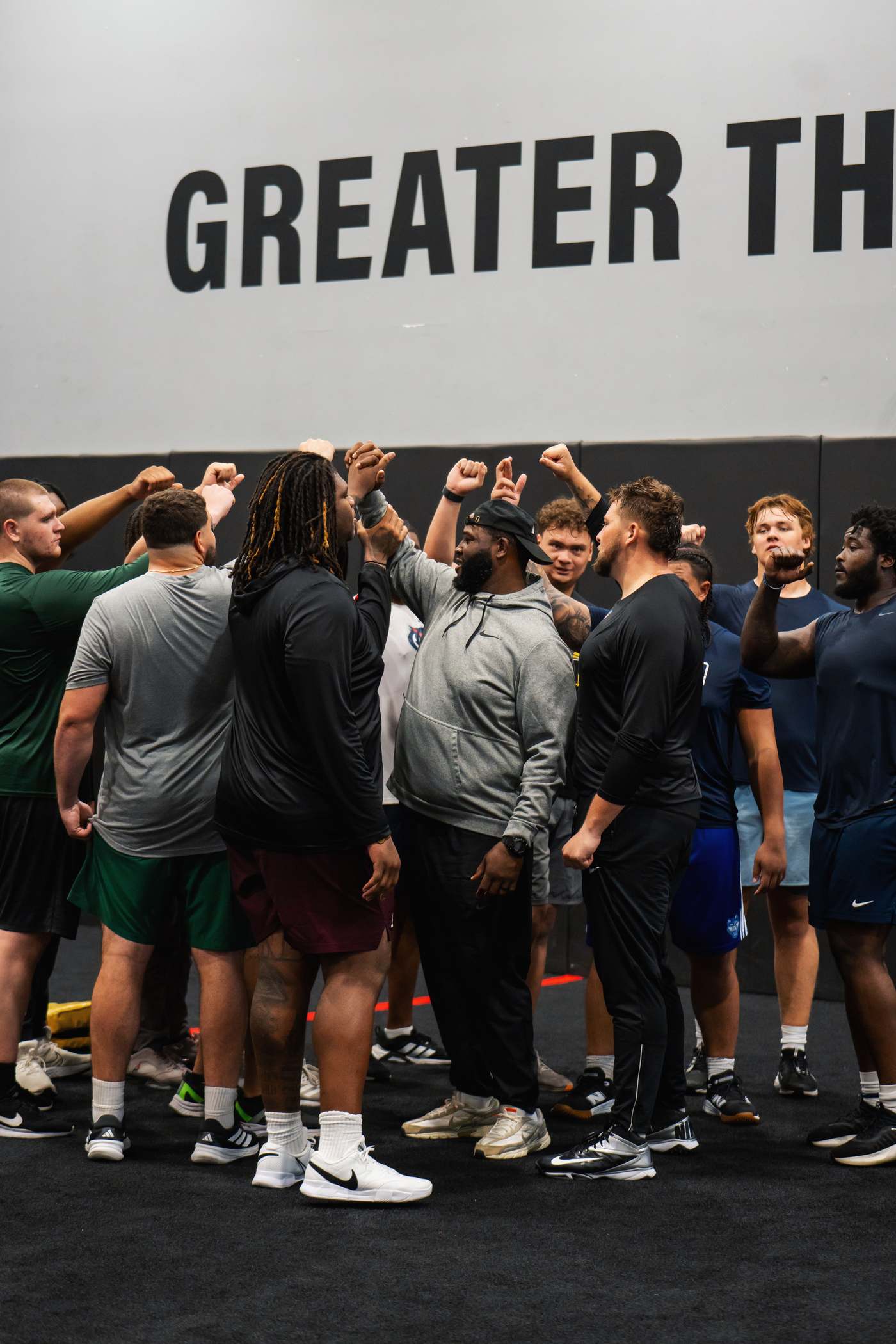 Wilson at the center of a Crafting Linemen huddle under the Greater Than wall